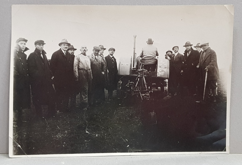 GRUP DE BARBATI ASISTAND LA LUCRARILE FACUTE CU TRACTORUL PE CAMP , FOTOGRAFIE MONOCROMA, PE HARTIE LUCIOASA , PERIOADA INTERBELICA , COLTURILE  DIN STANGA JOS INDOIT *